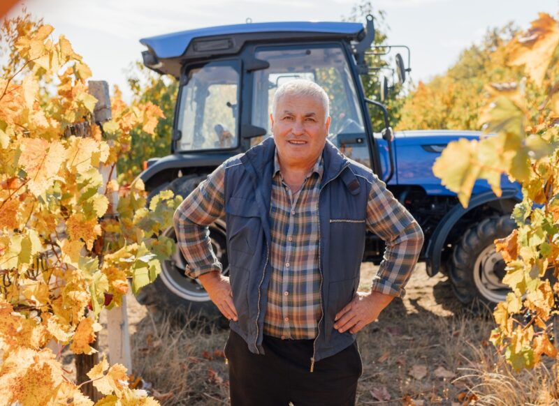 prikaz starijeg čoveka koji stoji u vinogradu, u pozadini traktor