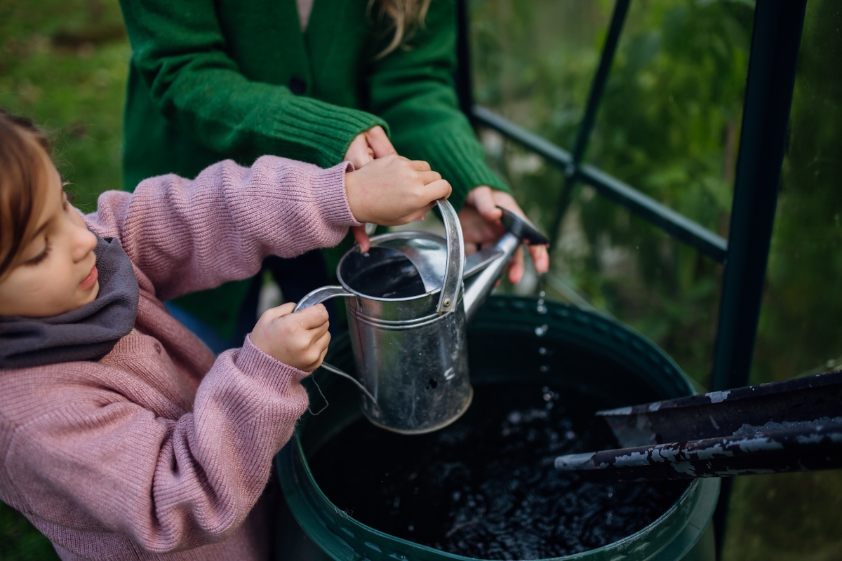 mama i ćerka uzimaju vodu iz bbureta sa kišnicom